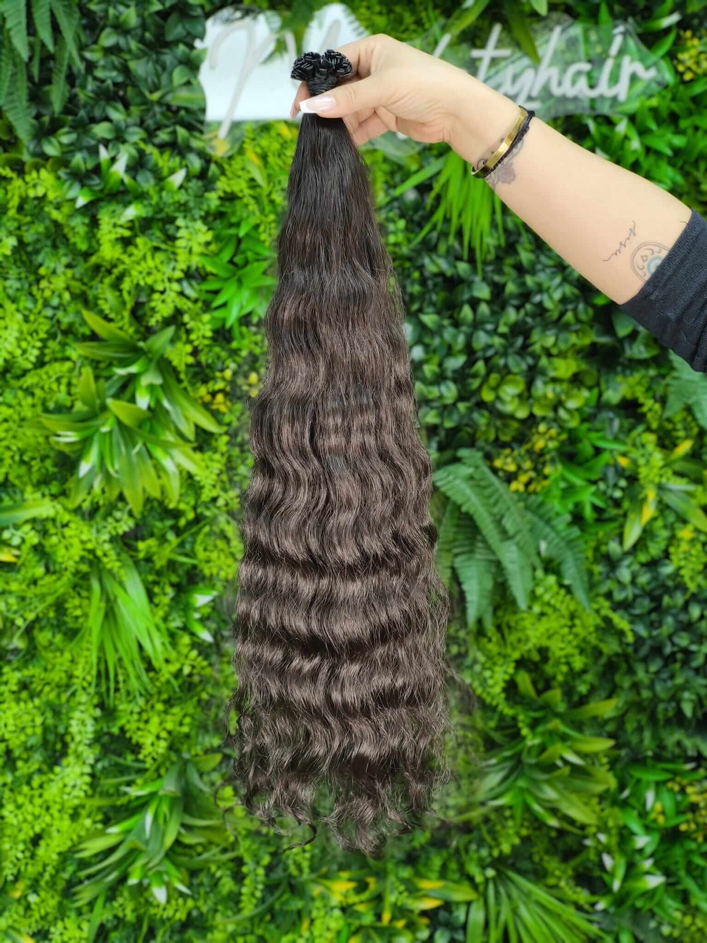 Virgin Echthaar Bondings dunkelbraun 66 cm, wellige Haarsträhne mit natürlichem Glanz auf grünem Hintergrund.