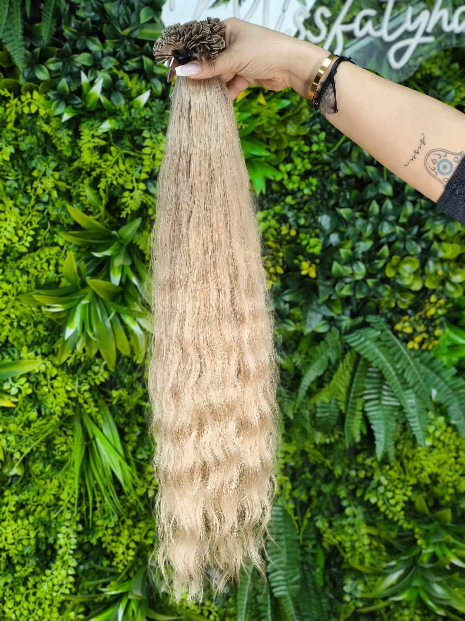 Virgin Echthaar Bondings 63 cm 188 g Hellblond wellig auf grünem Hintergrund